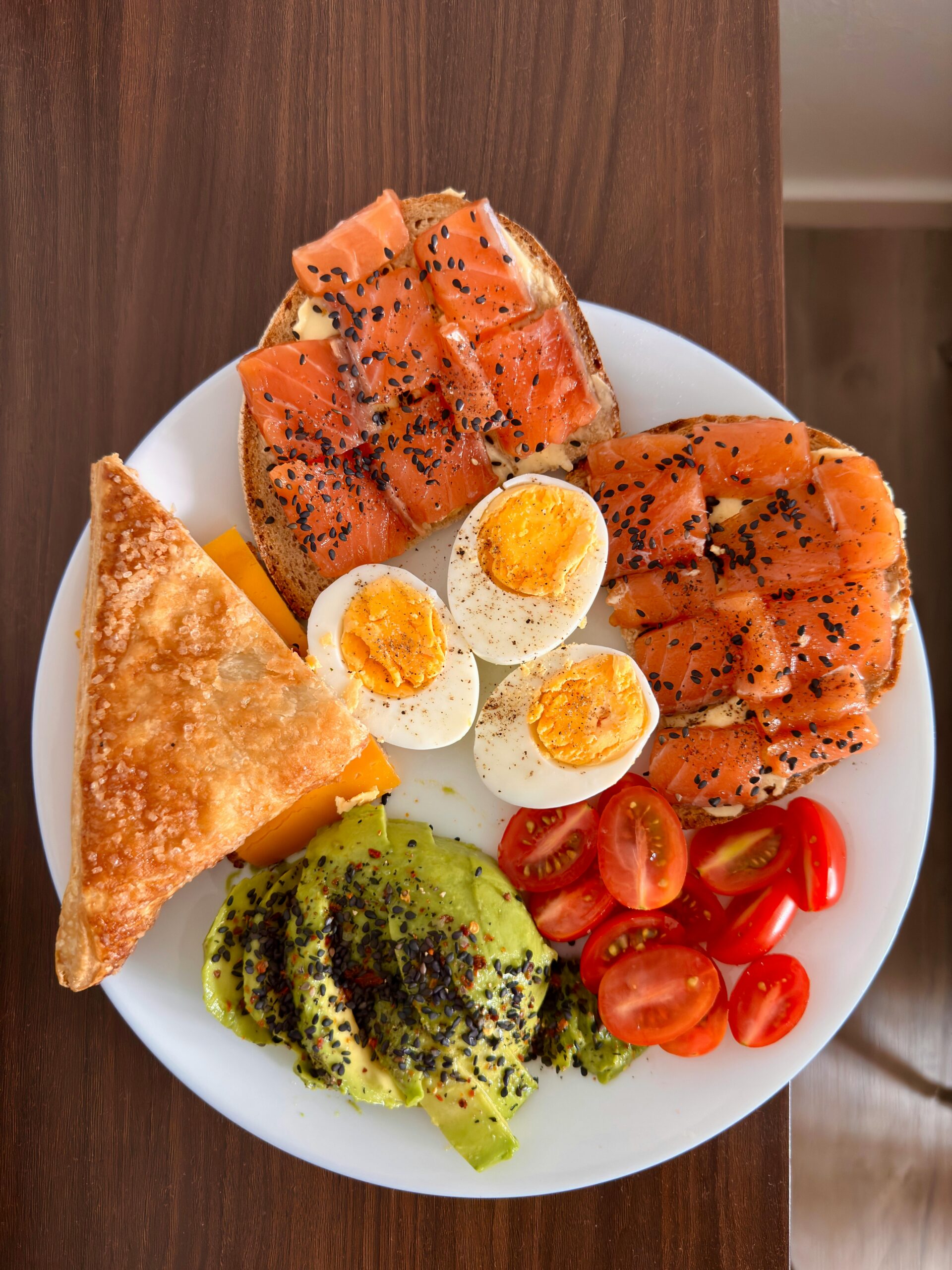 A vibrant breakfast platter featuring salmon, avocado, eggs, and tomatoes on a white plate.