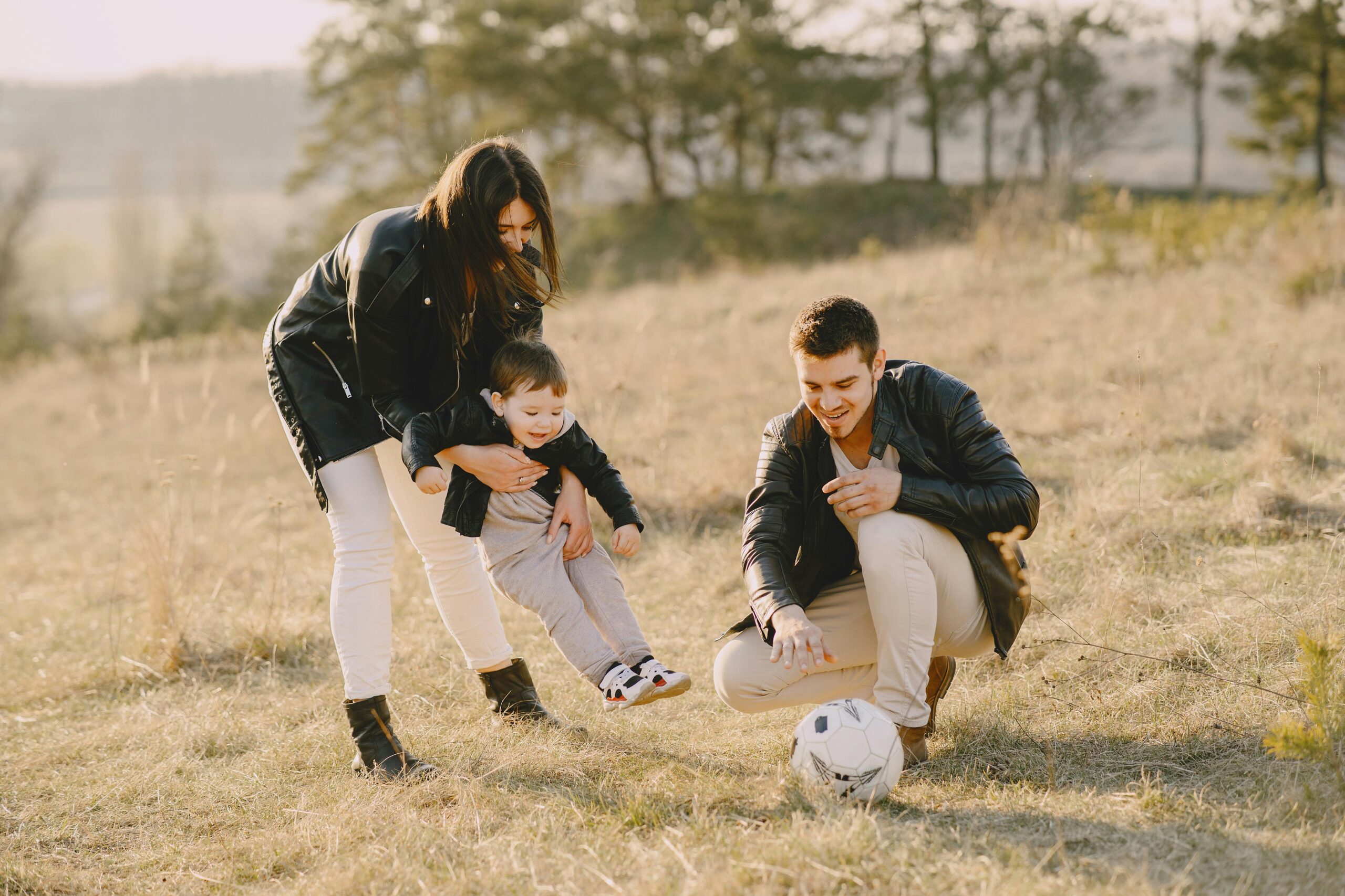 A happy family playing with a soccer ball in a grassy field on a sunny day.