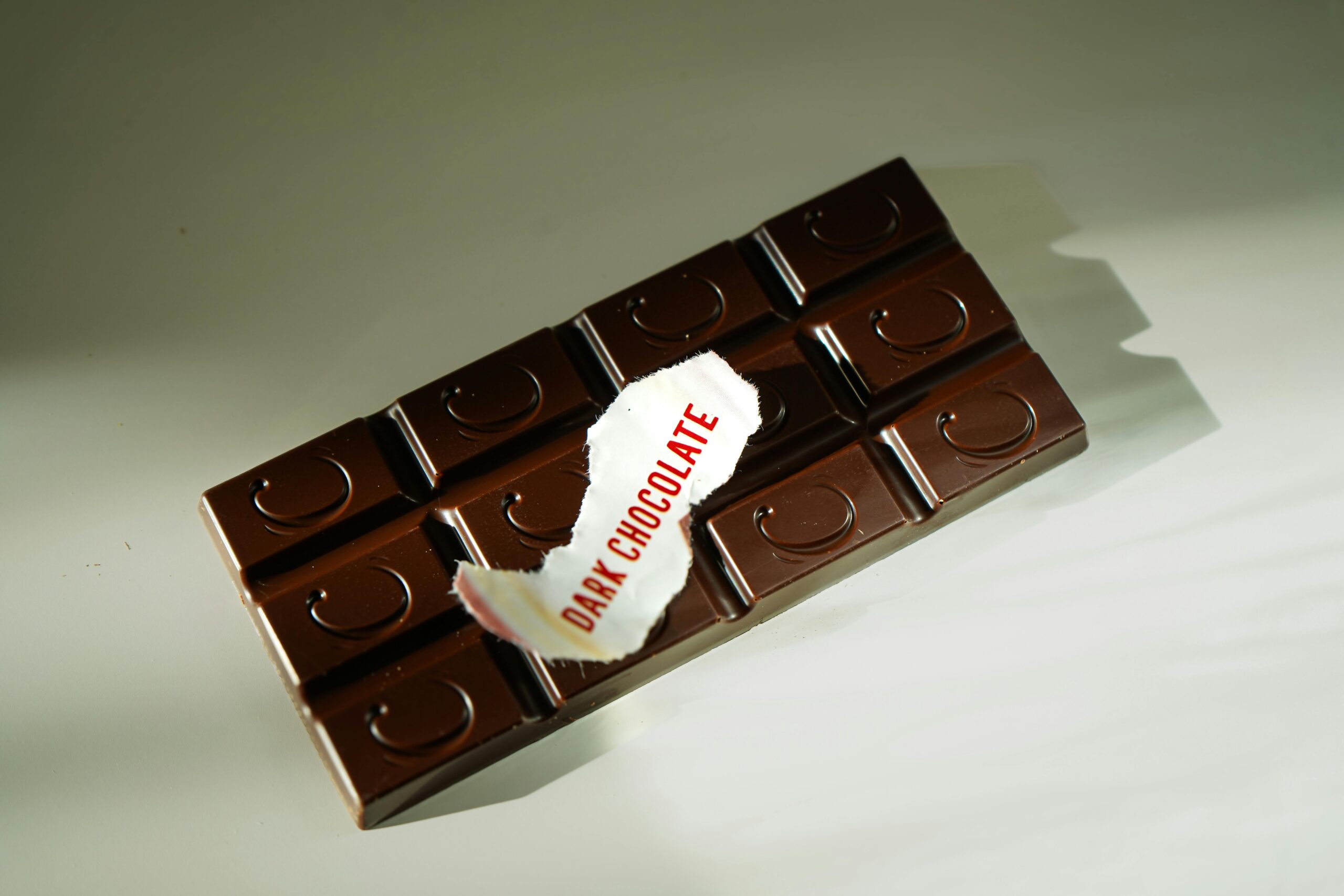 A dark chocolate bar with a torn label reading 'Dark Chocolate', photographed under natural light.