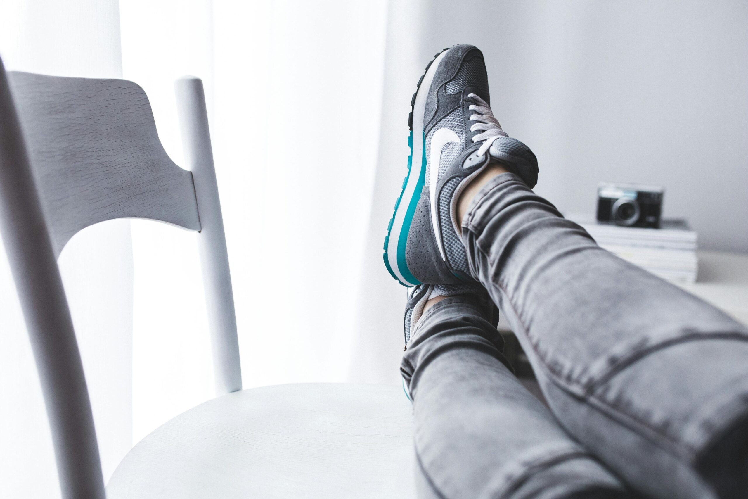A woman lounging with her feet up on a chair, showcasing grey sneakers.