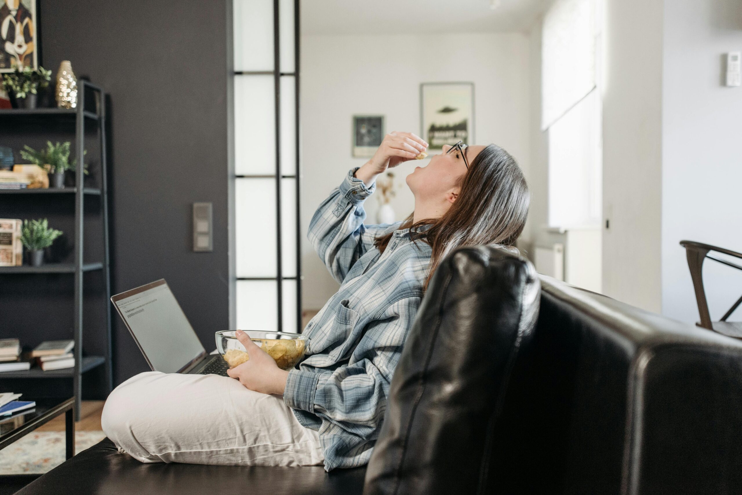 Woman enjoying snacks while working from home on laptop.