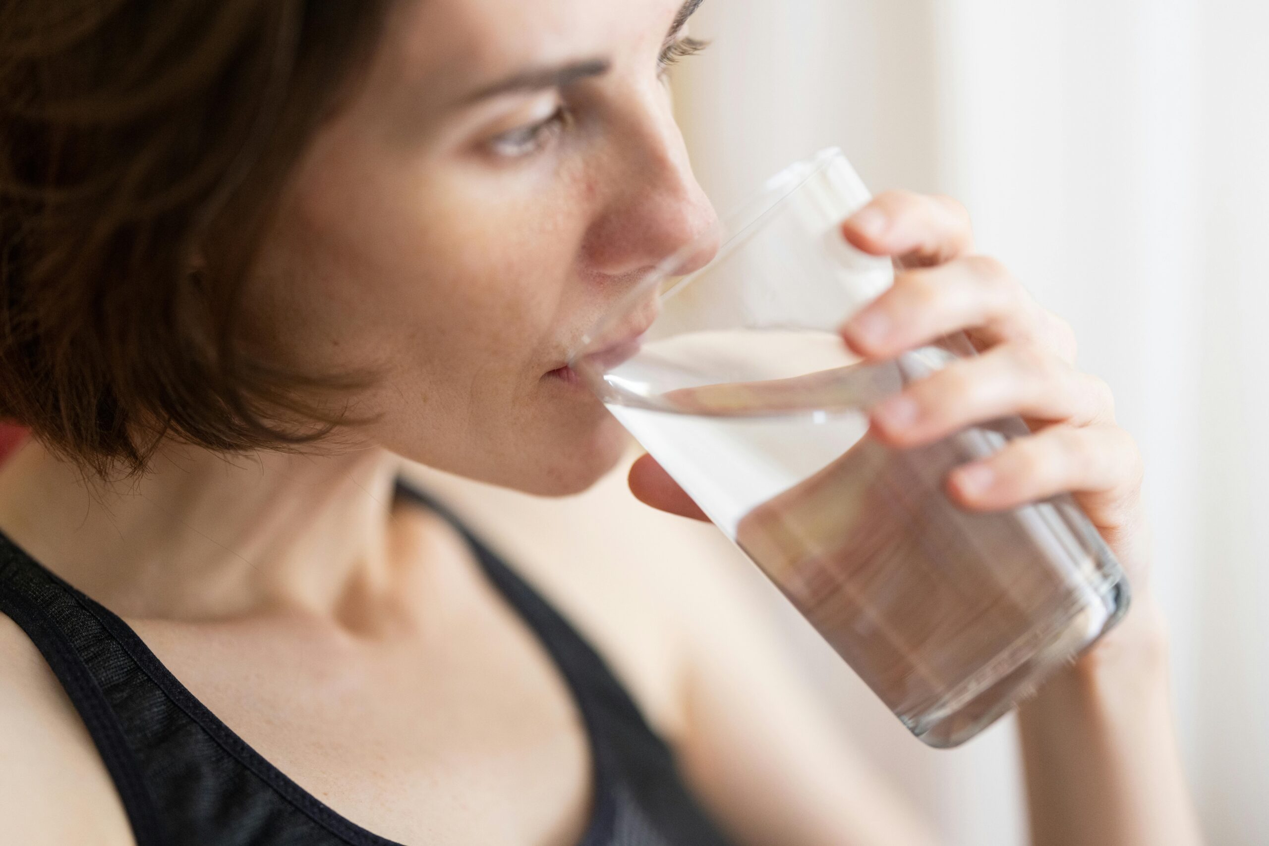 Close-up of an adult woman drinking a glass of water for hydration and health.