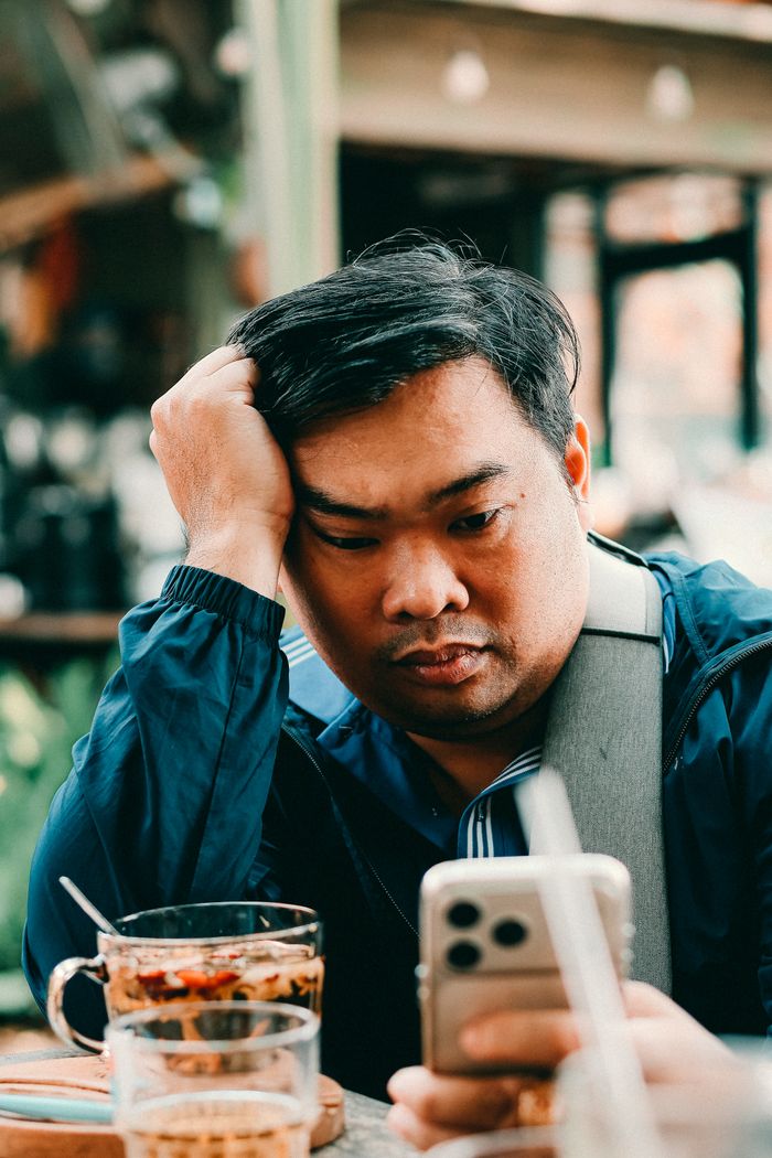 A man looks exhausted checking his phone in a cafe with drinks around. Captured in an indoor setting.