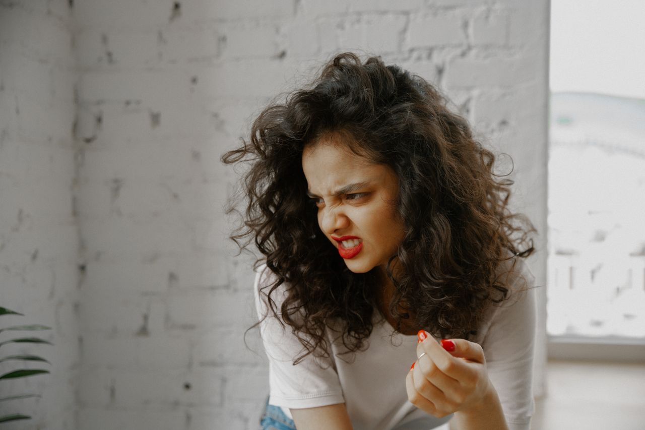 A woman with vibrant curly hair shows a strong expression of disgust.